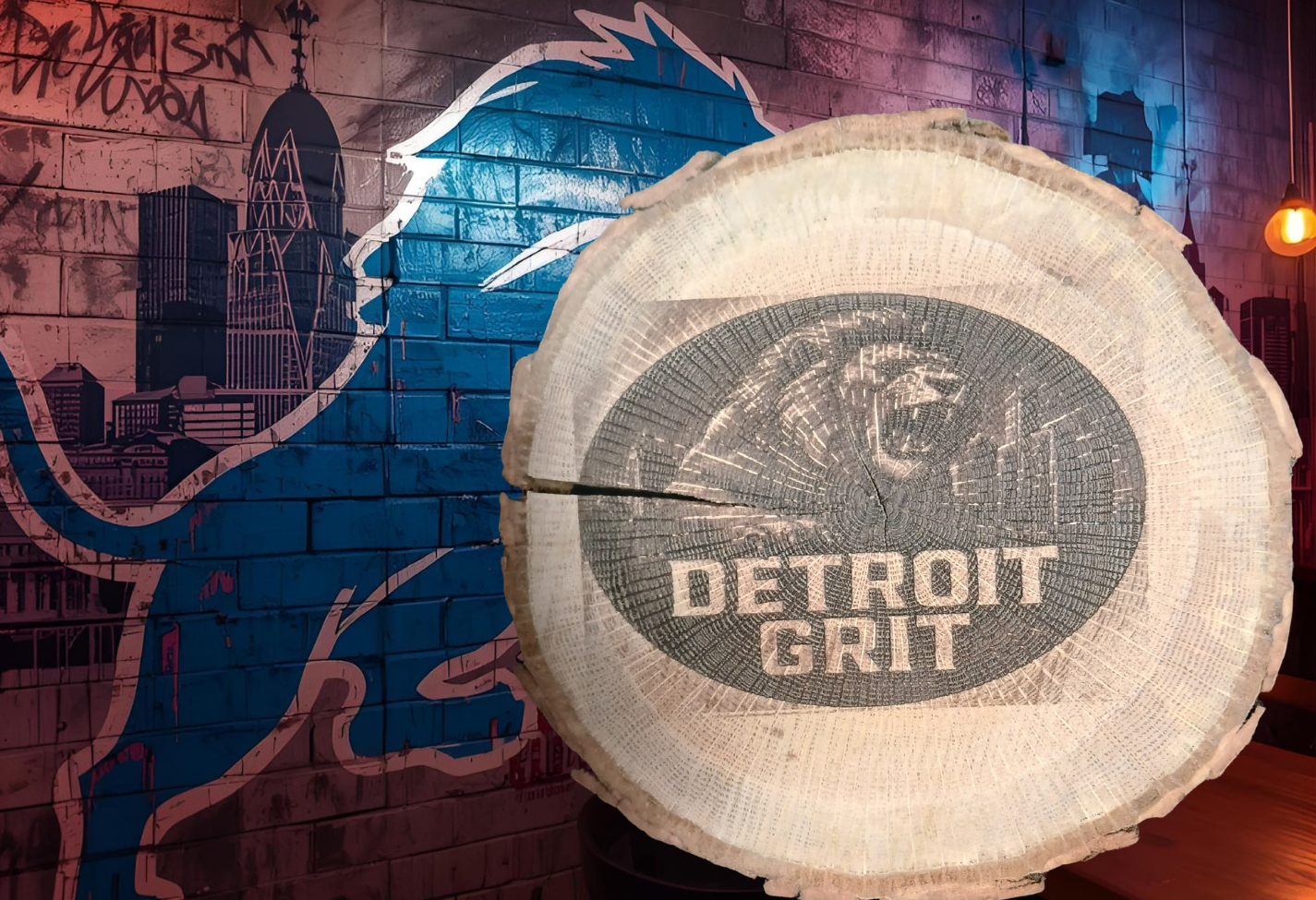 Wooden log with 'Detroit Grit' engraving against a graffiti-covered wall.